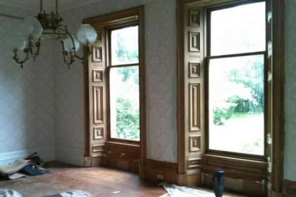 Room featuring two large windows overlooking a garden, with the walls stripped of paint