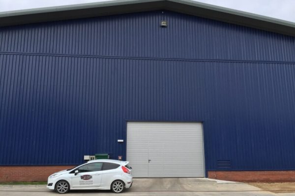 Large industrial shed building with fresh coat of dark blue pain, with a T Mone company vehicle parked in front