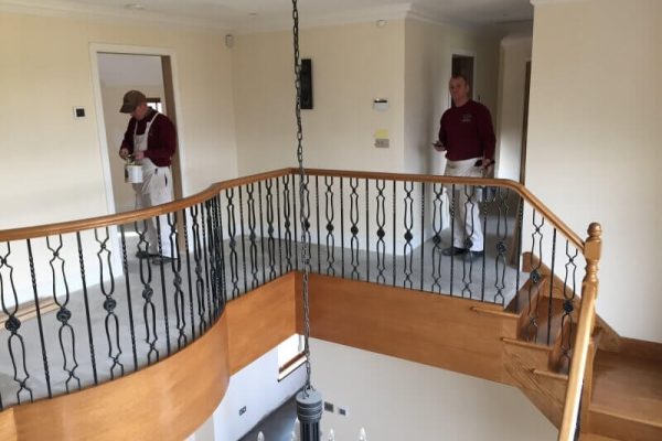 Two men undertaken painting and decorating work on second floor landing