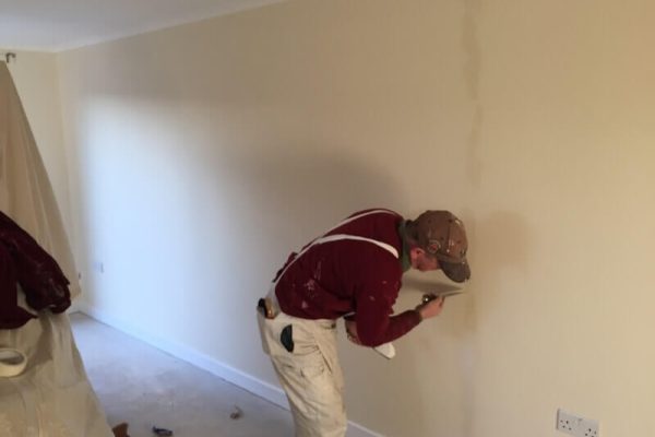 man in the process of painting a wall white. another person is slightly off screen